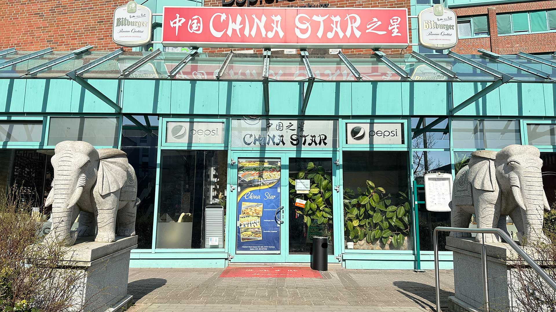 Außenansicht eines Restaurants mit zwei großen Elefantenstatuen; Glasfront und bunte Schilder.